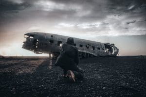 Man kneeling in front of a damaged aircraft fuselage.